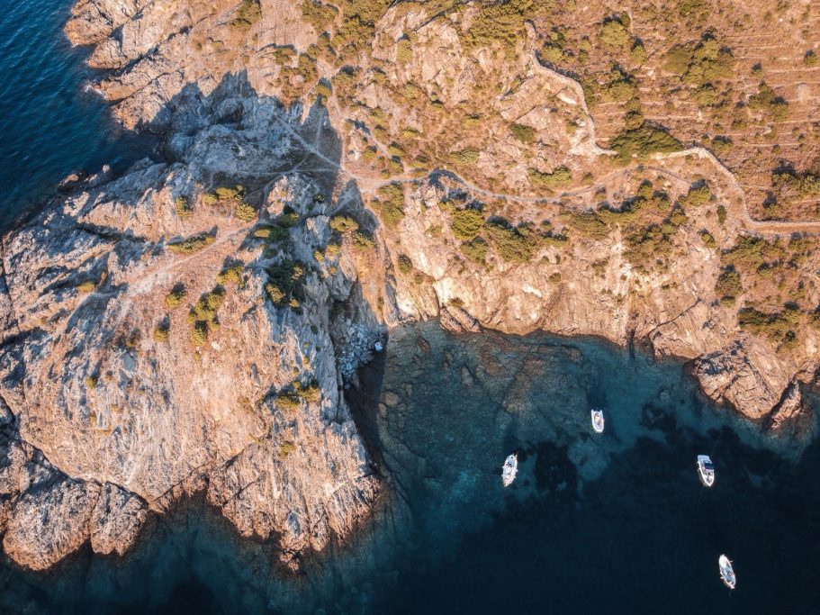 Vista aérea de una costa rocosa con botes en aguas claras cercanas.
